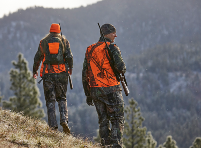 Two hunters in orange safety vests walking on a mountainside.
