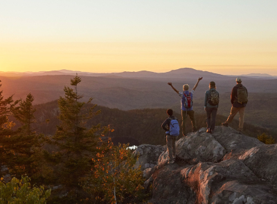 Sunrise with 3 people standing on a mountain top facing the sun