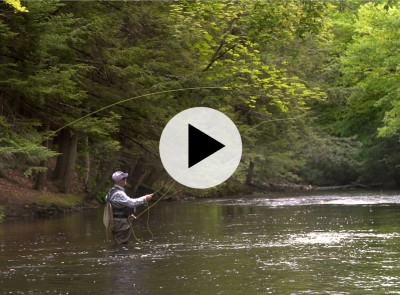 Man standing waist deep in a river fly fishing.