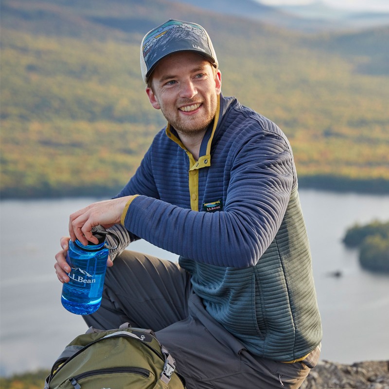 A man kneeling down at the top of a mountain holding a water bottle.