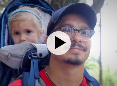 Smiling man with glasses with a child in a backpack.