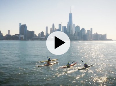 City skyline with four men kayaking in the foreground.