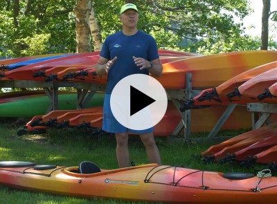 A kayak instructor outside with several kayaks, play video symbol in the center.