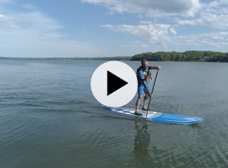 A man paddling a SUP on the ocean, a play video icon in the center.