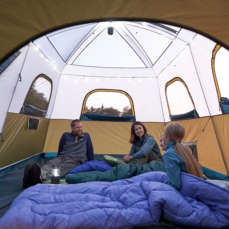 A man, woman, and two children sit inside of a tent with sleeping bags