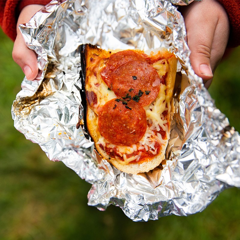 Hands holding french bread pepperoni pizza in alumninum foil