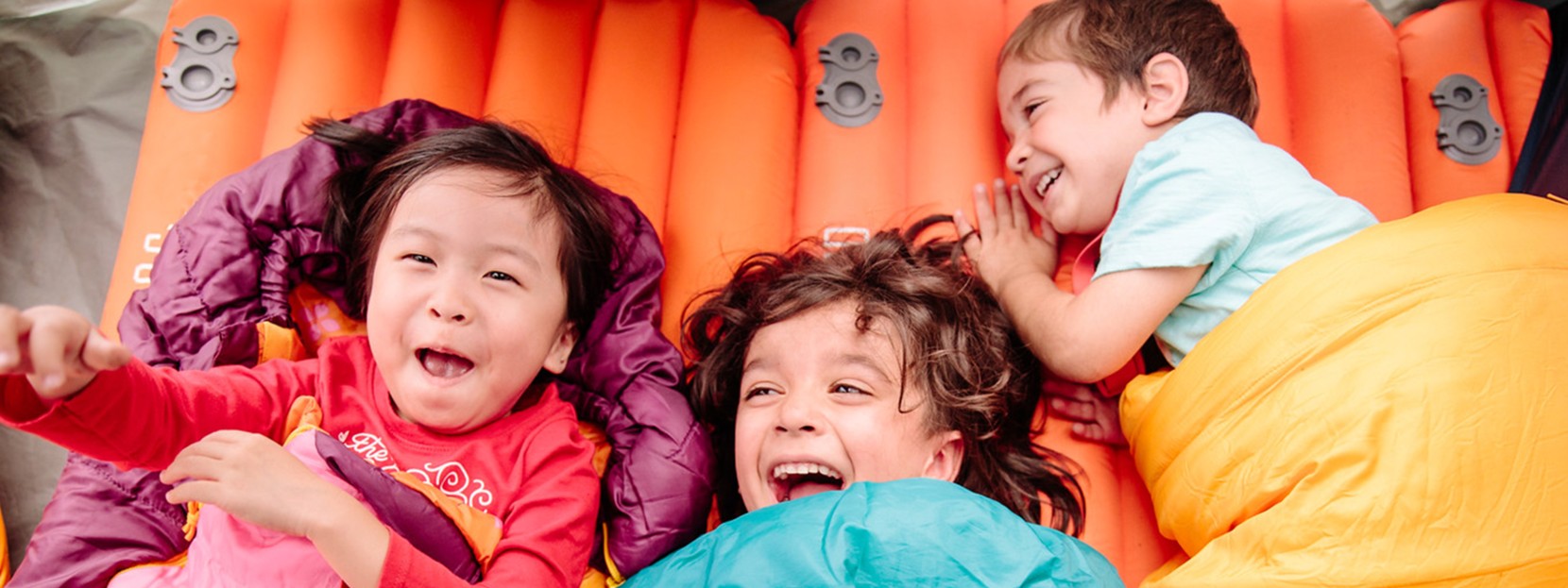 Three children laugh and lay in sleeping bags