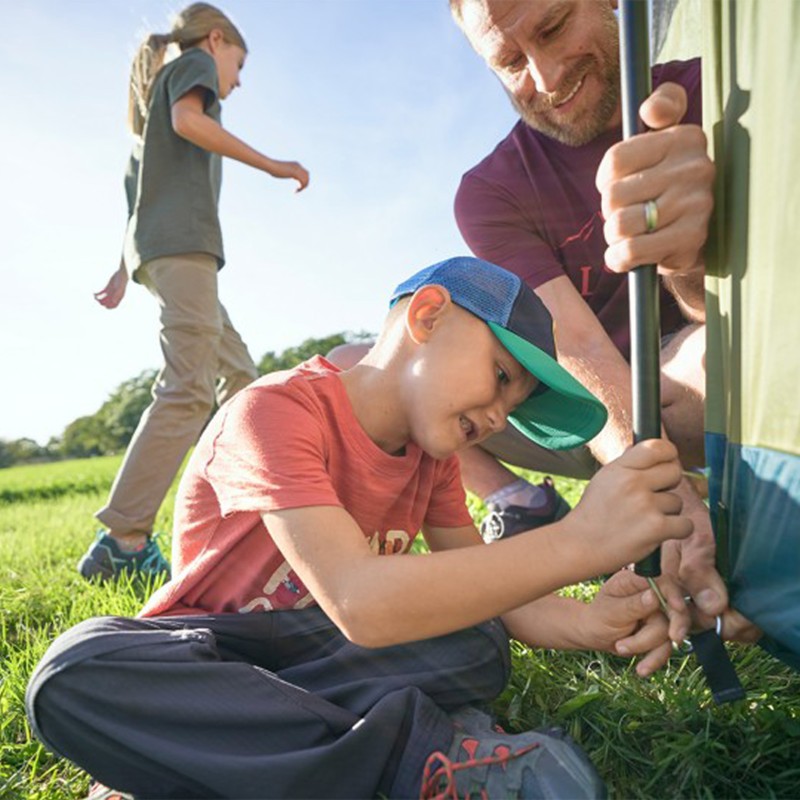 A man and child set up a tent, a girl walks by in the background