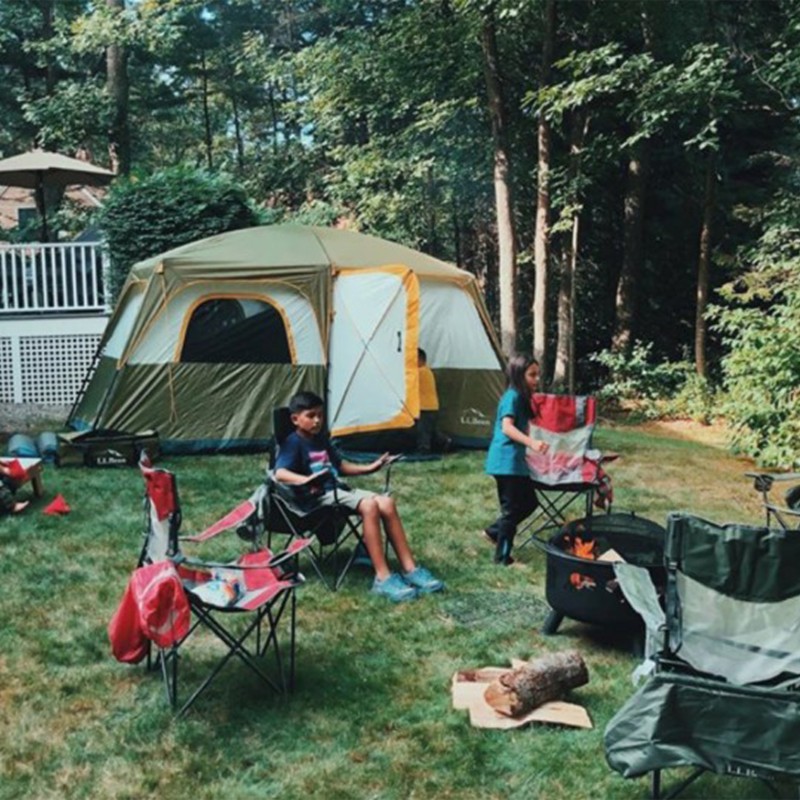 Tent and chairs set up in a back yard, children sit by a fire