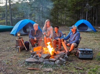 Family sitting around campfire, tents in the background.