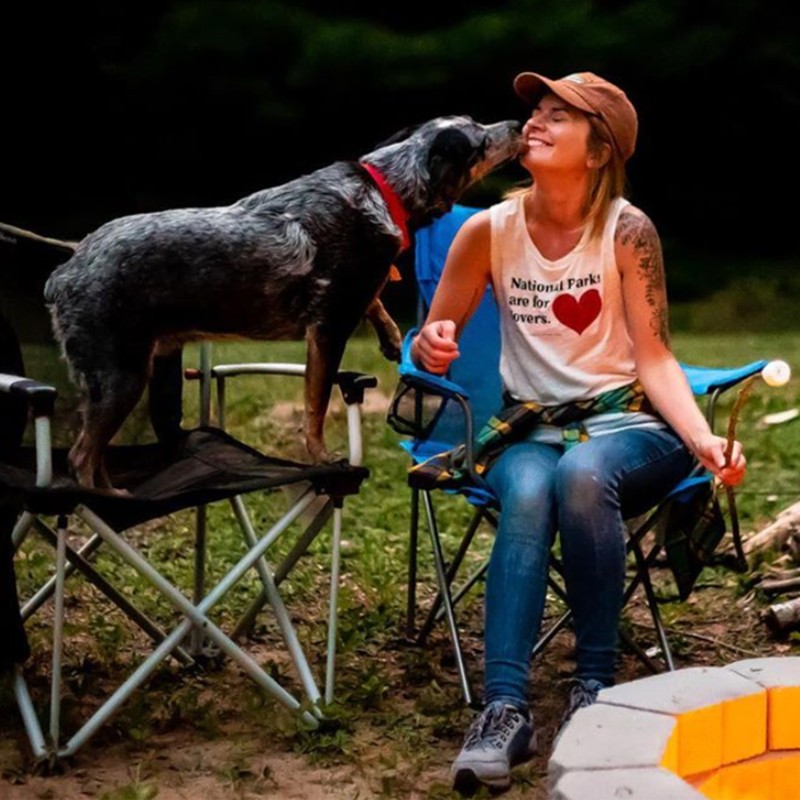 A dog and a woman on camp chairs, dog is giving the woman a kiss