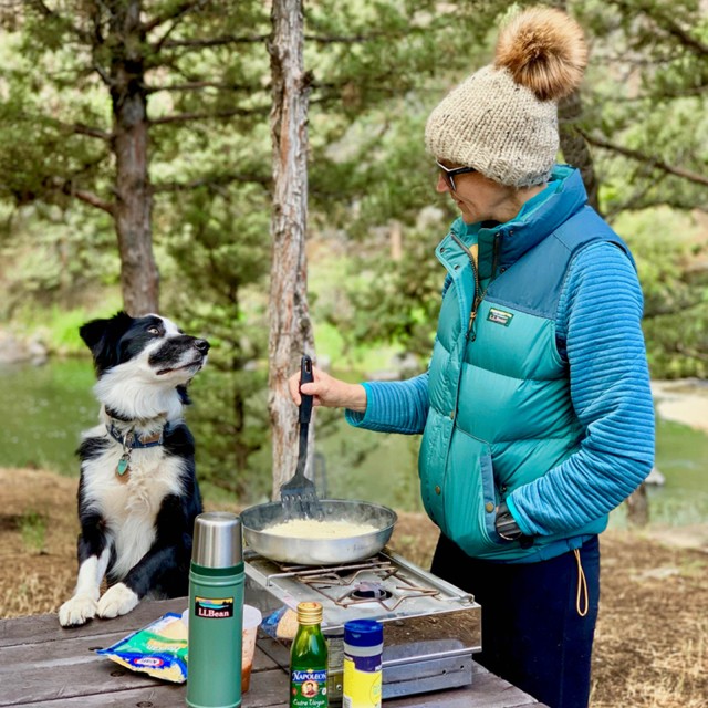 A woman making dinner outside at a campsite with her dog watching