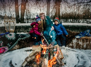 Two children and woman sitting in front of a fire roasting marshmallows in winter.