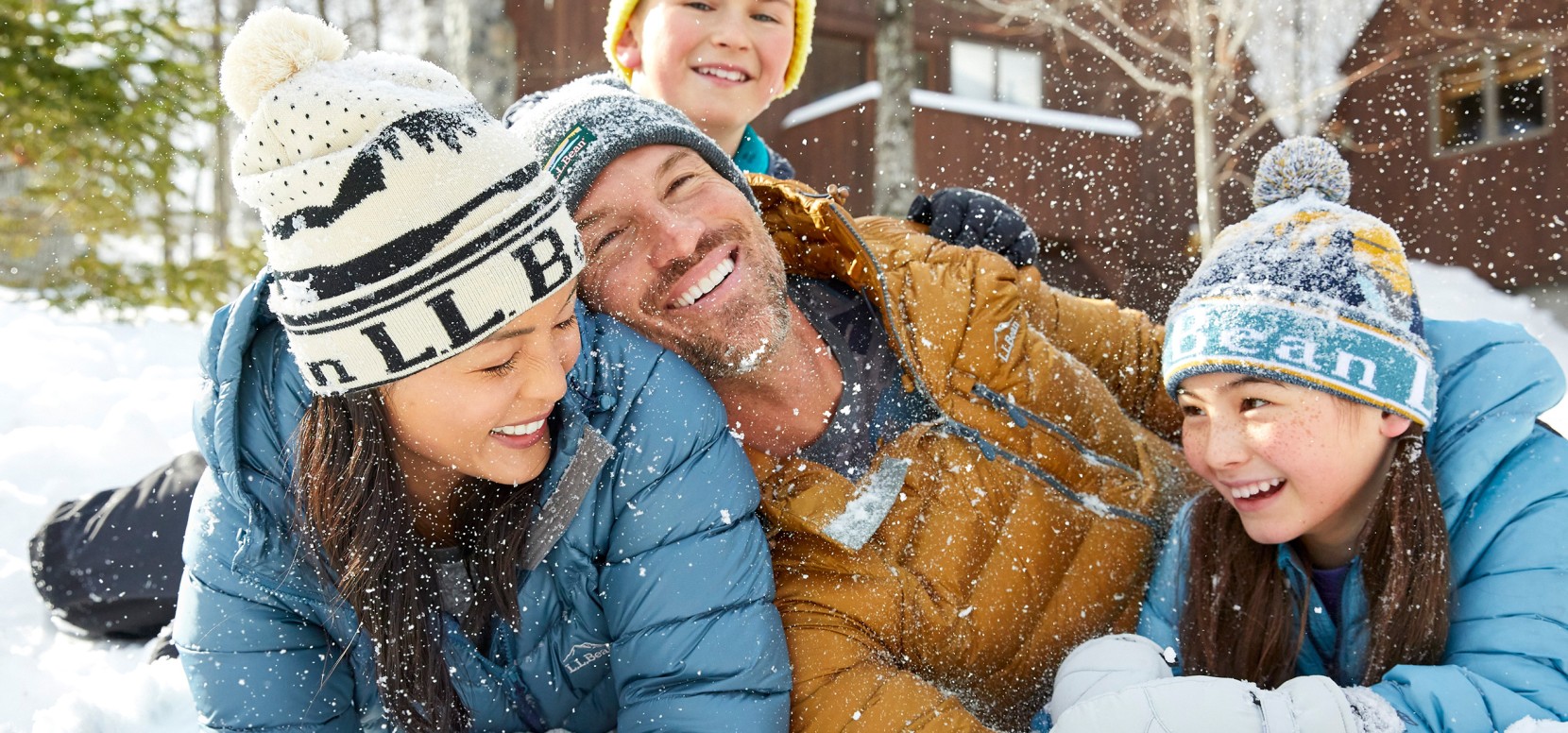 Happy family of three laughing on the ground in the snow.