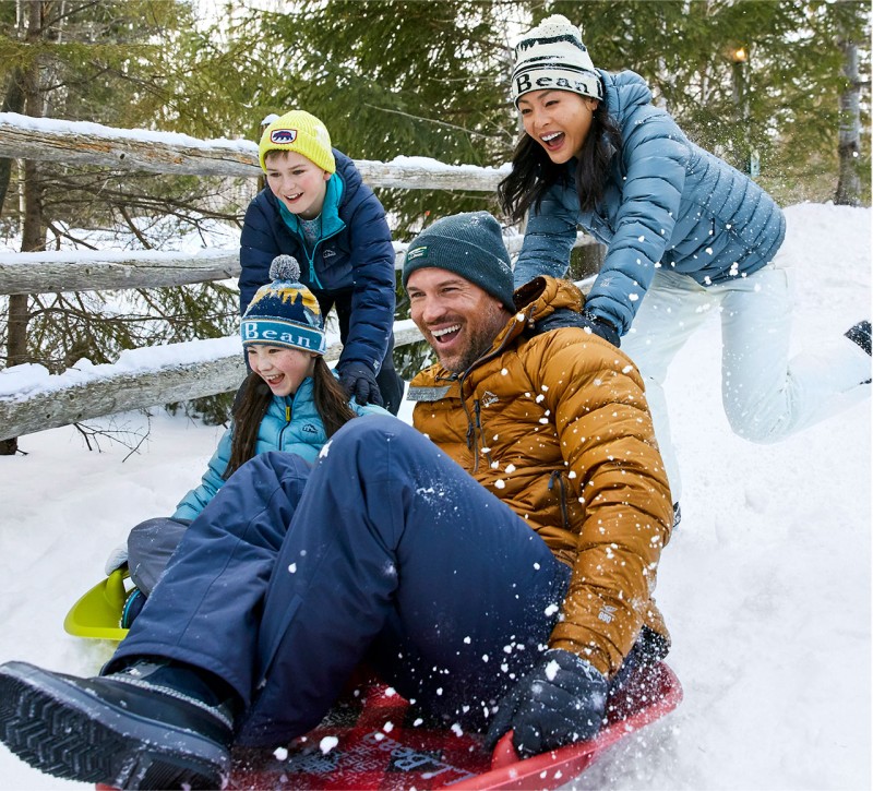 Family of 4 sledding and laughing outside in the snow.