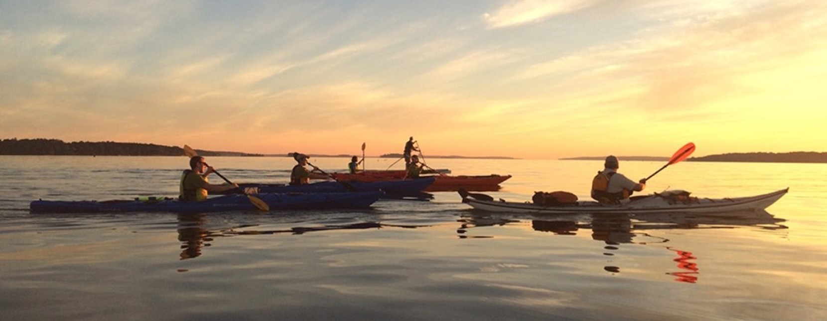 Several kayakers and a paddleboarder enjoying beautiful sky before sunset.