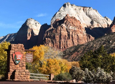 A beautiful rock formation against a bright blue sky with a Zion National Park entrance sign in the foreground.