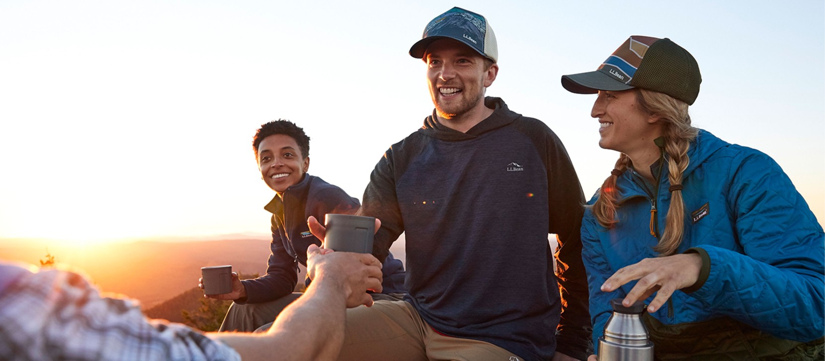 Friends drinking hot tea on top of a mountain as the sun begins to set.