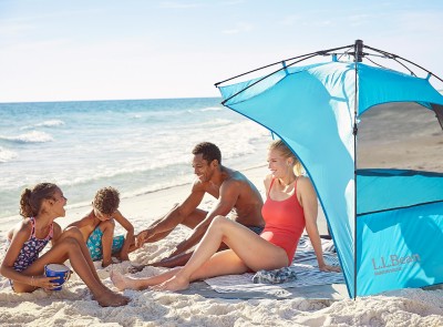 Family of 4 sitting in and around a sun shelter on the beach.