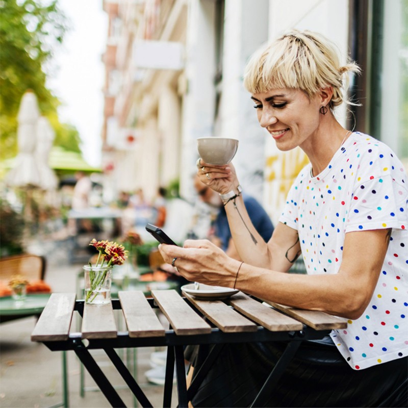 A woman drinking coffee at an outdoor cafe in the city.