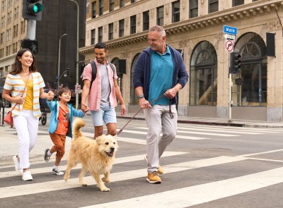 Family of 4 crossing the street in the city with their dog.