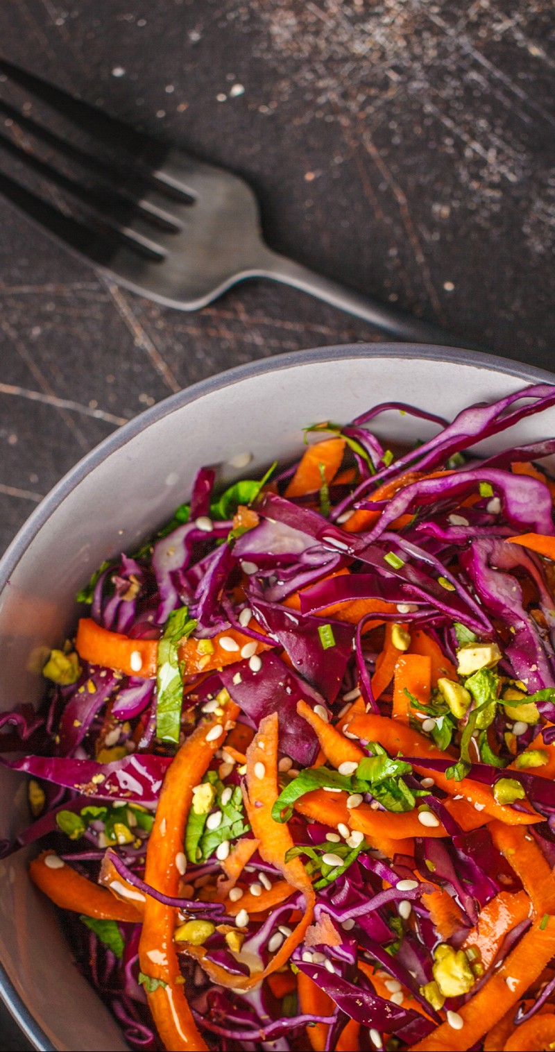 Colorful asian slaw in a white bowl on a dark stone slab.