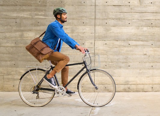 A man riding a bike in the city carrying a messenger bag.