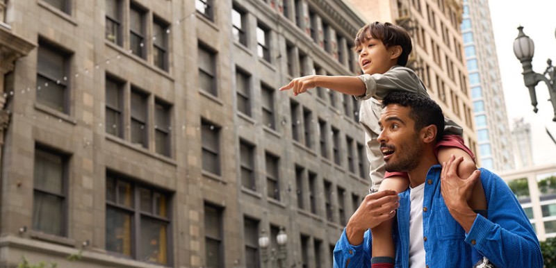 A man with a child on his shoulders walking in the city.