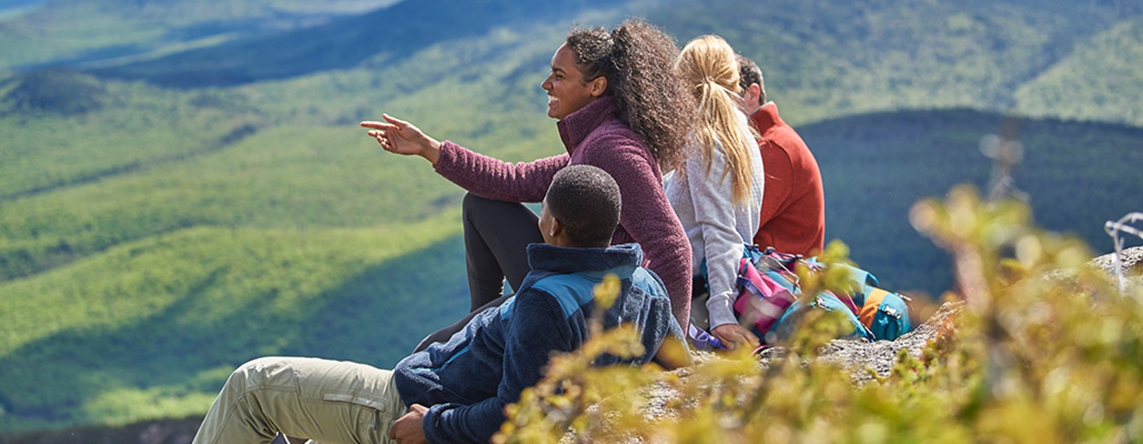 Group of people sitting, looking out over a mountain landscape.