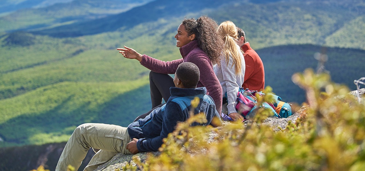 Group of people sitting, looking out over a mountain landscape.