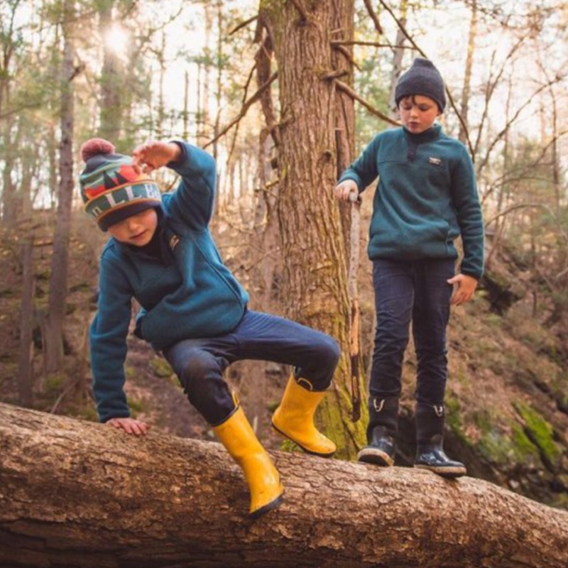Two kids playing on a log in the forest