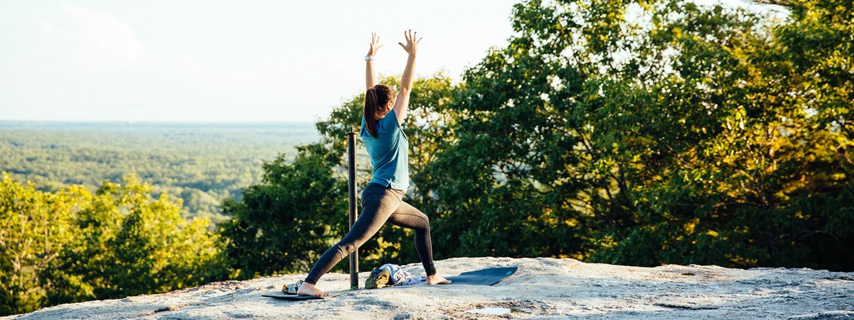 A woman in a standing yoga pose on top of a mountain.