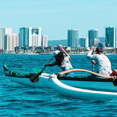 Photo of people paddling with a city view in the background.