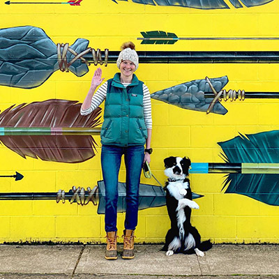 A woman standing with her dog in front of a wall mural.
