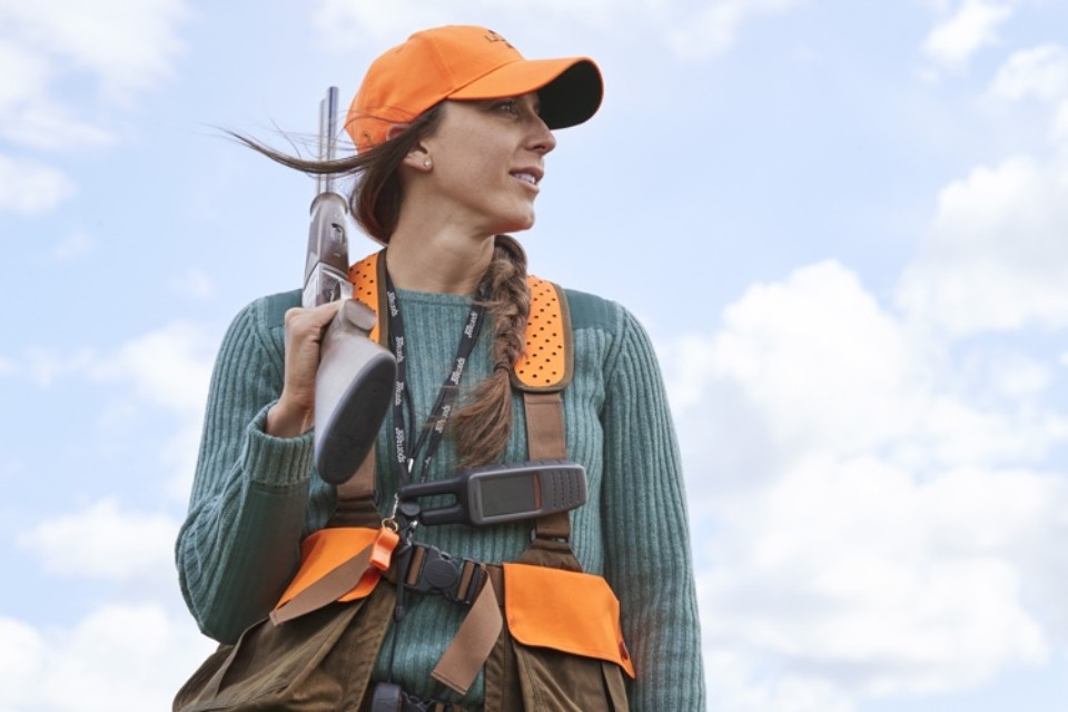 Upward shot of Christi Holmes wearing hunting gear, framed by blue sky and puffy white clouds.