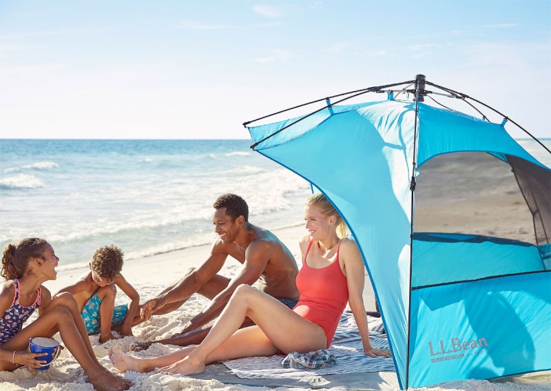 A family of 4 relaxing in and around a sun shelter on the beach.