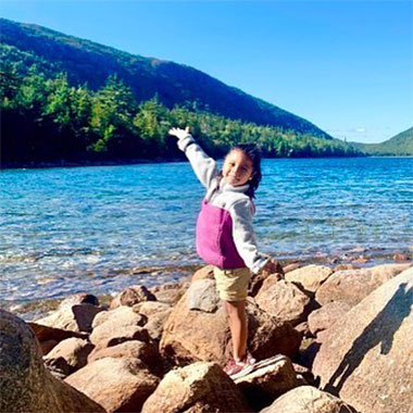 A little girl with arms spread wide by a beautiful lake.
