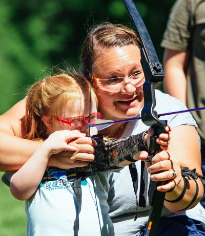 A mom helping her daughter with a bow and arrow