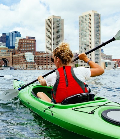 A woman kayaking with a city view in the background
