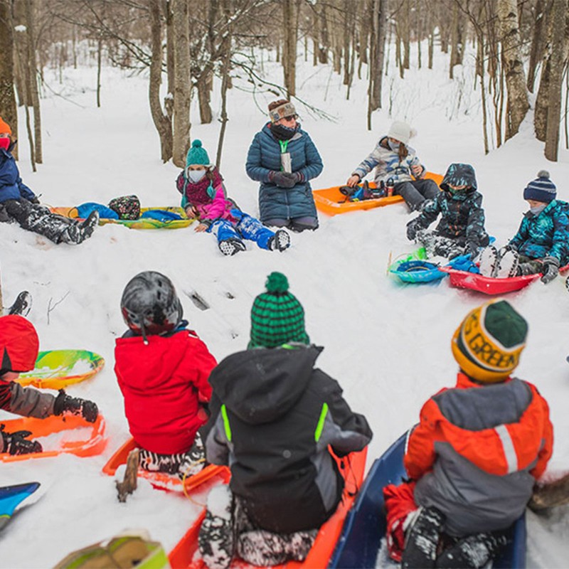 Students and teacher outside in winter, sitting on sleds in a circle.