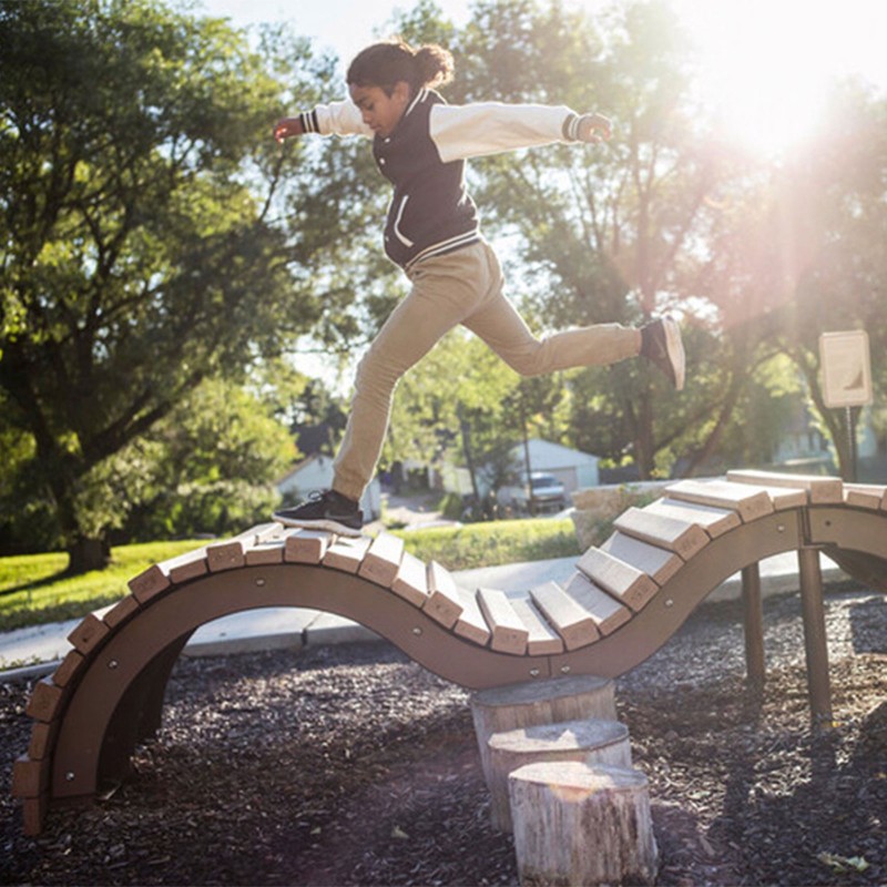 Young girl leaping across a curvy playground structure.