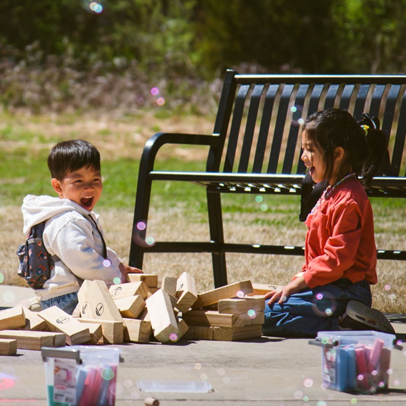 2 kids playing outisde with blocks, bubbles and chalk.