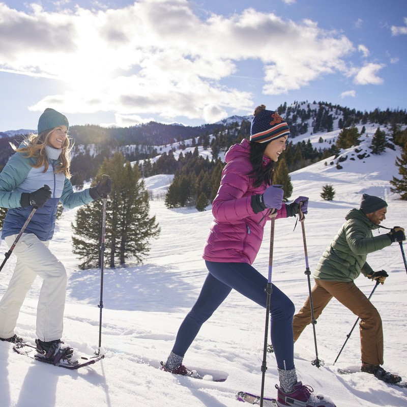 3 people snowshoeing in a beautiful field surrounded by mountains.