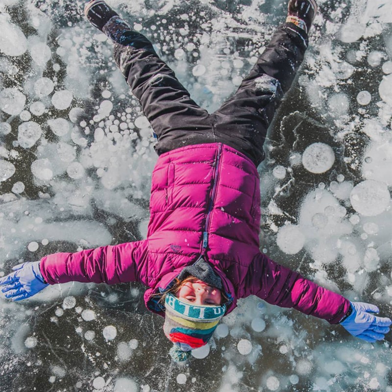 Looking from above, a child laying on a frozen pond.