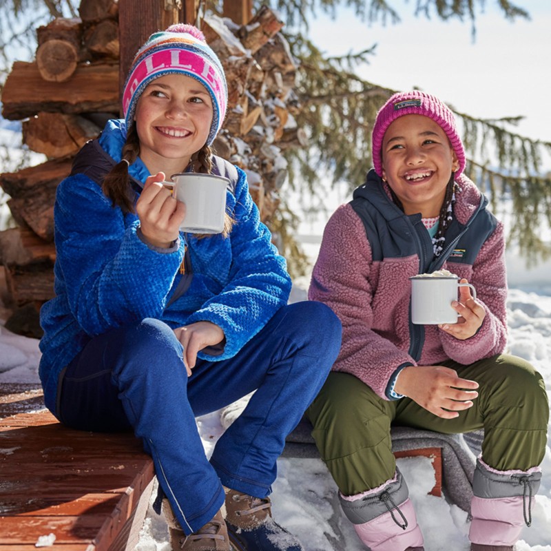 2 smiling kids sitting on a snowy porch enjoying hot cocoa.
