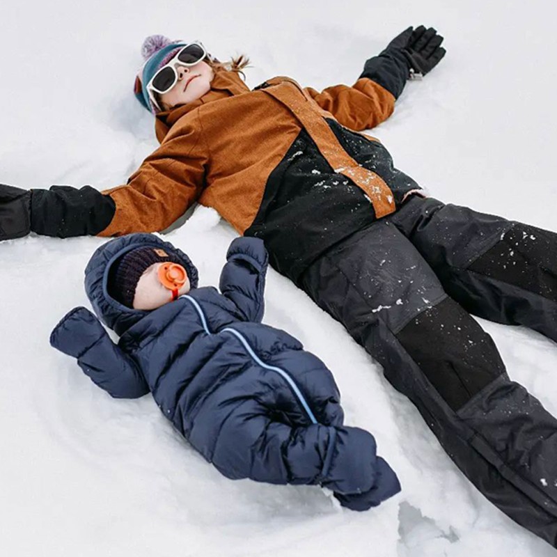 A child teaching a toddler to make snow angels.