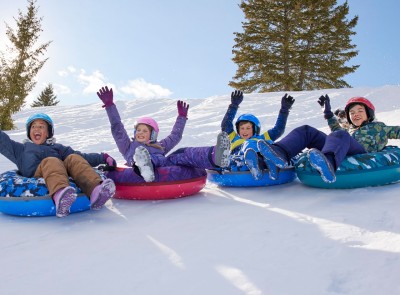 4 kids on Sonic Snow Tubes sliding down a snowy hill, arm up in the air.