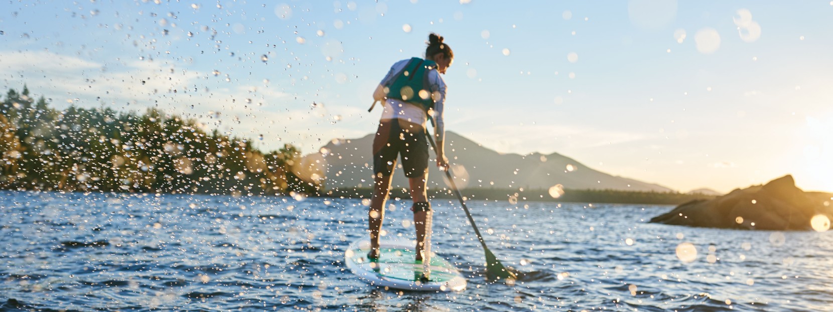 A woman paddling a stand up paddle board toward the shore.