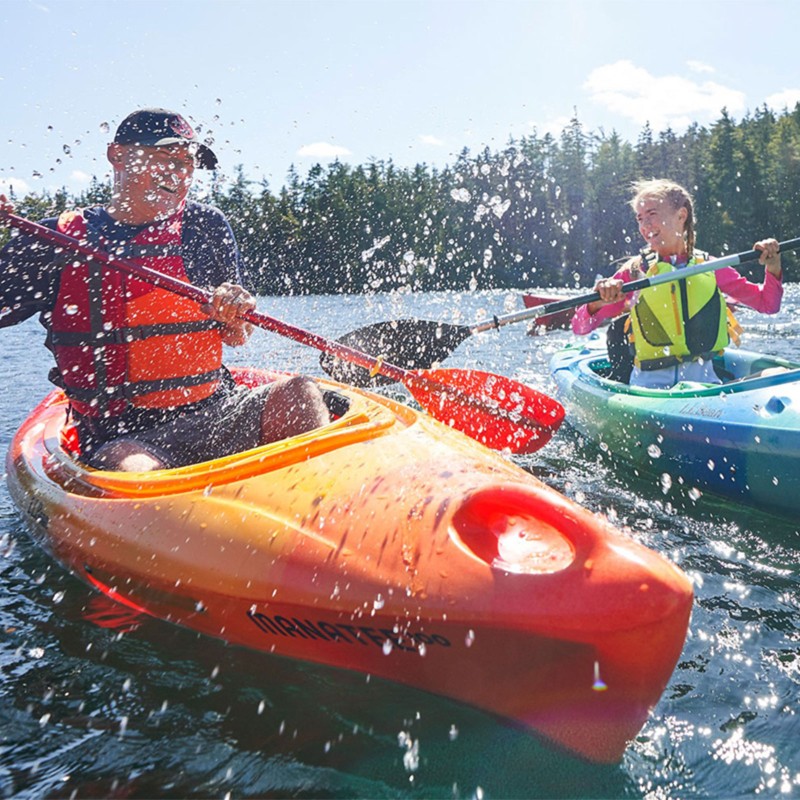 2 smiling kids in kayaks splashing each other.