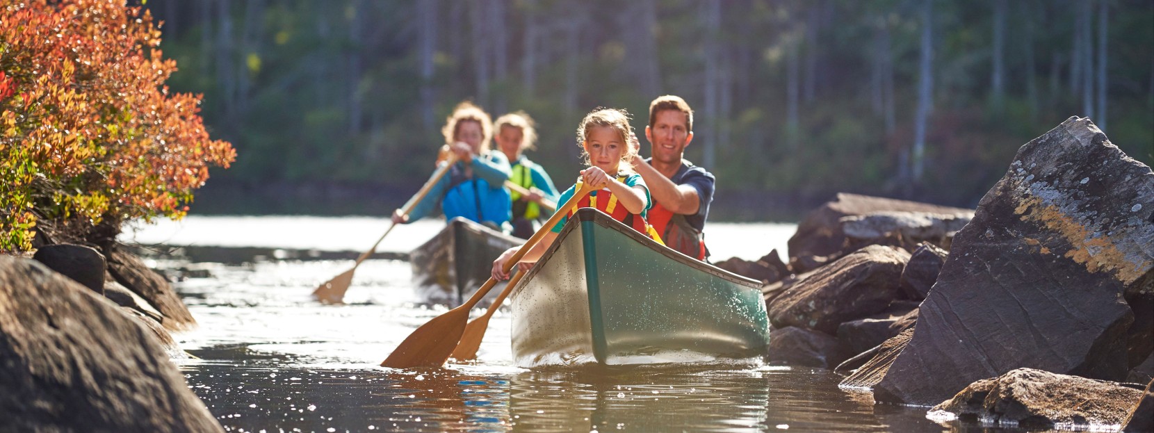 A family of 4 in 2 canoes paddles toward the camera.